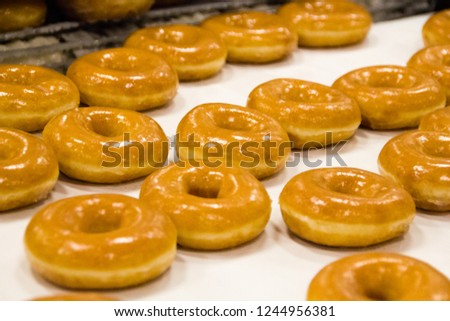 Detail of a doughnut production business with freshly baked donuts coming out of the oven. Royalty-Free Stock Photo #1244956381