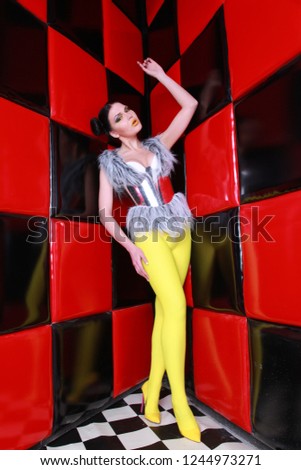 crazy fashion girl wearing yellow pantyhose, silver furwaistcoat and futuristic steel belt posing near red wall with black squares alone