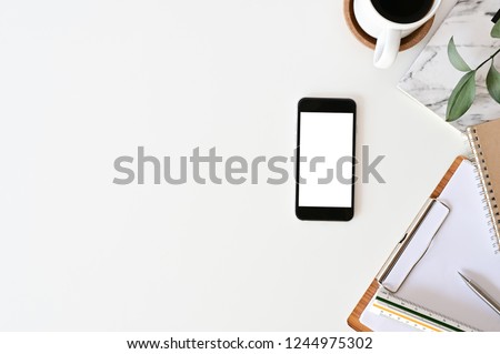 Top view office desk. Workspace with mockup smartphone, keyboard and office supplies, pencil, green leaf with coffee on white background.
