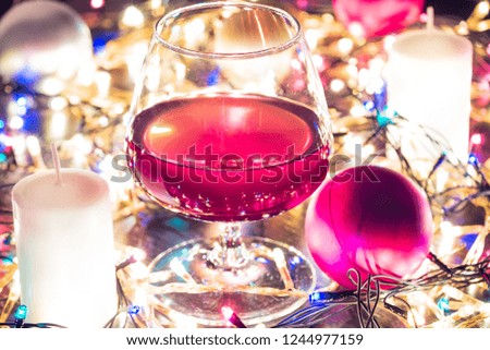 Candles, Christmas balls, garlands on a Christmas background and a glass of brandy close-up. Bokeh effect
