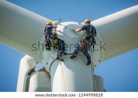 Inspection engineers preparing to rappel down a rotor blade of a wind turbine in a North German wind farm on a clear day with blue sky. Royalty-Free Stock Photo #1244998828