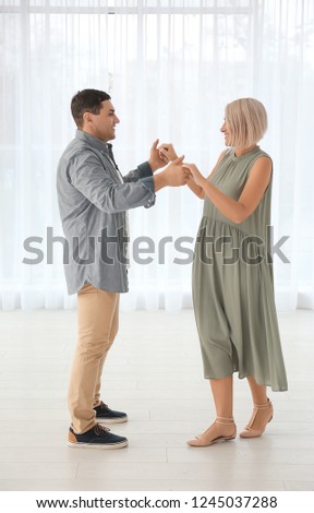 Adorable mature couple dancing together indoors against window