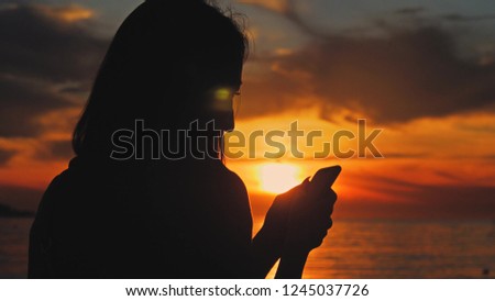 Silhouette of young tourist woman use phone during sunset in ocean beach. Always connected, the concept of Internet technology.