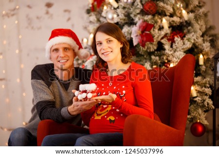 Photo of cheerful men in Santa cap with gift and pregnant woman