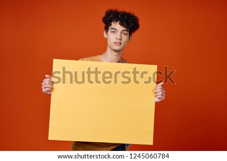 A man with curly hair is holding a yellow mockup                  