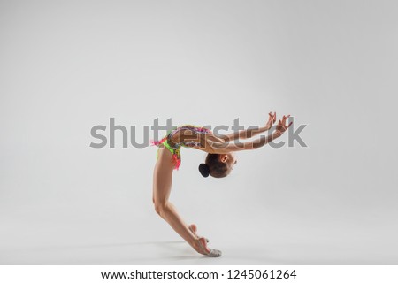 The teen female little girl doing gymnastics exercises isolated on a gray studio background. The gymnastic, stretch, fitness, lifestyle, training, sport concept