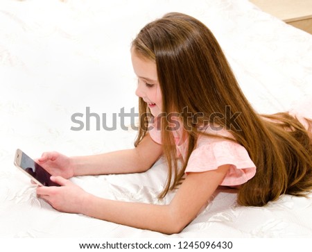 Cute smiling little girl child with her mobile phone smartphone lying on the bed technology and internet concept 