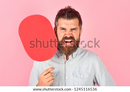 Hipster with angry face holds red nameplate. Feeling and emotions. Face expression, life perception. Wrathful bearded man with cardboard in hand. Evil man with empty name card. Man with beard&mustache