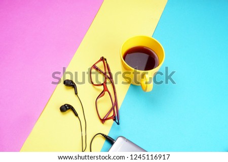 Top view of colorful working table have Headphones,mobile phone and cup of tea on color blue, Yellow and pink background for create idea for business or design. Relax time listen song (flat lay).