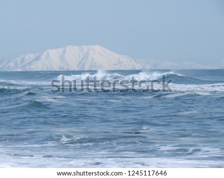 The shore of the Pacific Ocean, waves and views of the snow-covered hill in winter in sunny weather in Kamchatka, Russia