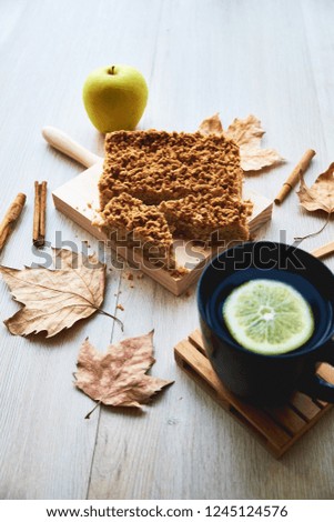 Delicious apple pie with autumn leaves, cinnamon and cup of tea with lemon on wooden background. Autumn composition with homemade cake.