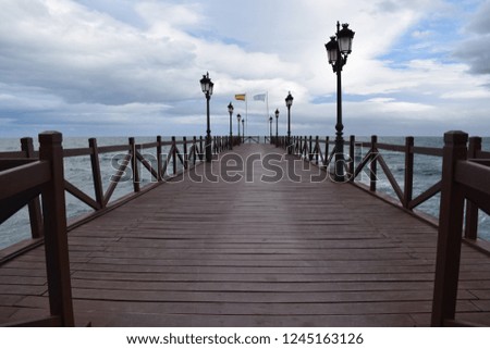 Really long shot with depth of a dock in Spain. There is a really cloudy sky. 