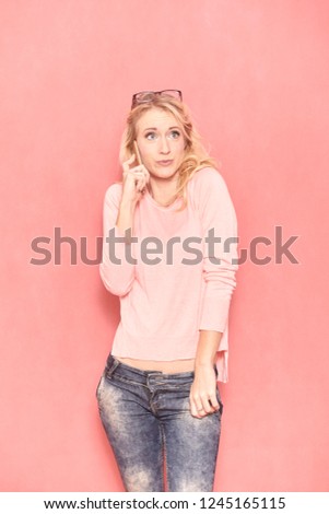 one young cute woman posing and talking over phone, looking sideways, 20-29 years old, long blond hair. Shot in studio on pink background.