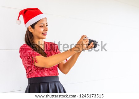 The beautiful Southeast Asian woman takes photos, dressed in red shirt , black skirt and red hat on Christmas festival.