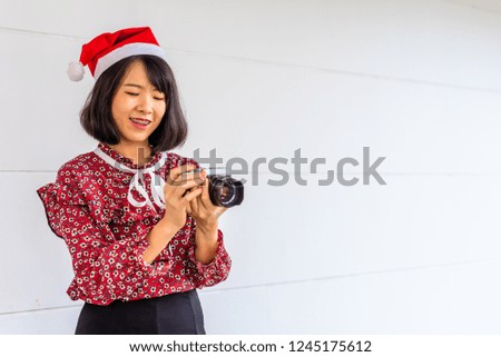 The beautiful Southeast Asian woman takes photos, dressed in red shirt , black skirt and red hat on Christmas festival.