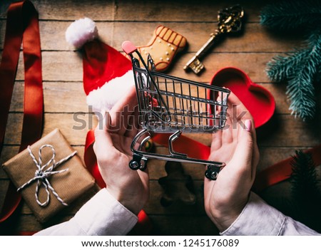 Hands holding Shopping cart with Cristmas gifts on background