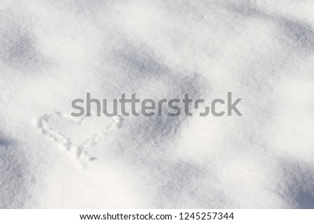 Symbol of heart on the background of fresh snow texture. Romantic heart shape made in fresh snow. Heart shape drawn in natural pattern. Happy Christmas, New year and St. Valentine day.
