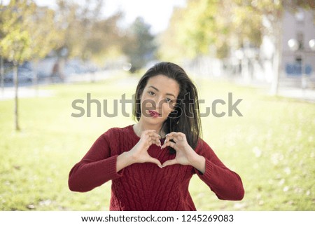 Beautiful young woman standing outdoors smiling in love showing heart symbol and shape with hands. Romantic concept