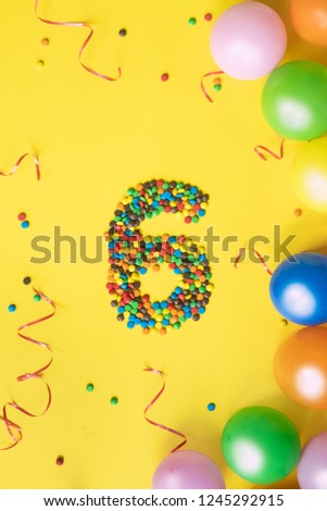 Candies number 6 with colorful balloons on yellow background. Concept for birthdays.