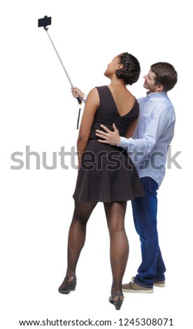 Back view of an interracial couple that makes selfie on selfie stick. beautiful friendly girl and guy together. Rear view people.  backside view of person.  Isolated over white background.  