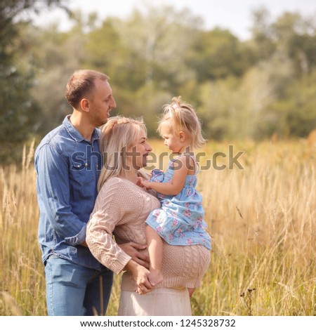 Portrait of pregnant pretty woman with her young husband and little cute child hugging and walking in park. Happy family waiting for a baby
