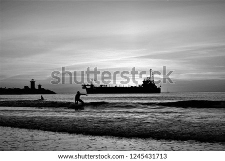 Black and white picture of ship and surfer on the ocean.
