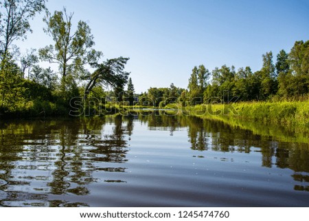 summer day on water in calm river enclosed in forests with sandstone cliffs and dry wood. dark water in river of Brasla, Latvia