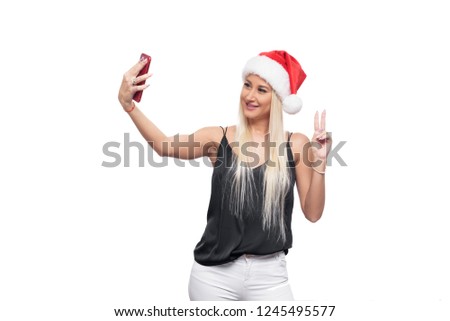 Smiling happy blond woman in black blouse and christmas santa hat make selfie on red smartphone camera over isolated white background. Sale concept