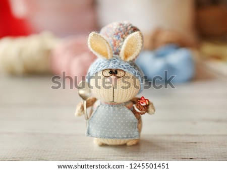 Handmade knitted toy. Easter Bunny pastry in a light blue apron holding in her paws sweet cake
