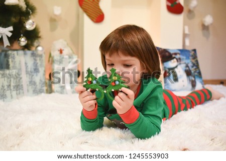 Little boy in New Year pajama lies in front of fireplace and Christmas tree. Boy wait a New Year