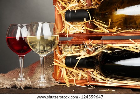 Wooden case with wine bottles and wineglasses on grey background