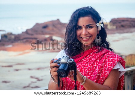 Female India photographer photographing with digital camera on the beach.beautiful indian woman in red traditional sari in the tropical paradise sea taking pictures of the landscape photo shoot