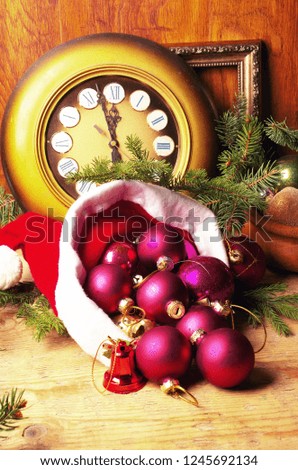 New Year's still-life. The clock with the arrows on the number twelve, Santa Claus's hat and colored balls on a wooden table.