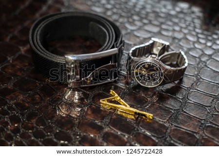 Men's accessories on a dark background: belt, watch, tie clip close-up.