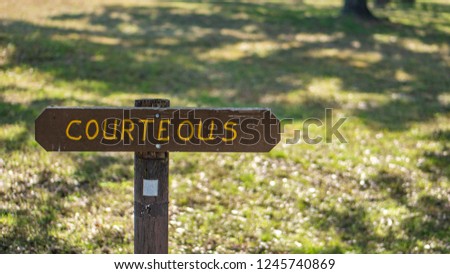 Brown wooden sign in grassy field with courteous written on it