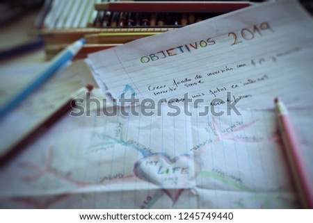Closed view of lined up papers with colored pencils around with new years resolutions. Title translation: Goals 1019. Text translation: Create an investment Fund; Invest 5000 euros; Sell my pictures