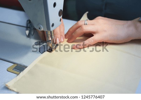 A woman sews on an electric sewing machine. Black material. Smooth seam.