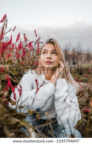 Blond hair smiling girl sitting in park near red flowers