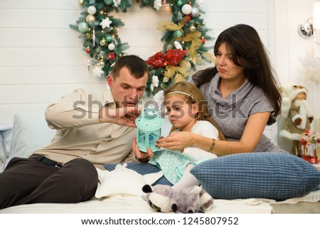 Happy family portrait on Christmas, mother, father and child sitting on bed and lighting a candle at home, chritmas decoration around them