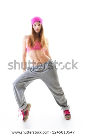 Full-length portrait of carefree girl in gray pants, pink top and hat jumping and dancing. Teen girl hip-hop dancer, over white background.