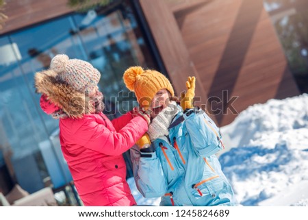 Mother and daughter on a winter vacation spending time together outdoors girl playing trying to take off woman's hat laughing surprised close-up