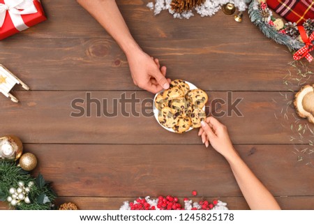 New year theme man and woman sharing plate of chocolate chip cookies isolated on decorated wooden table top view close-up