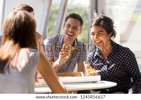 Indian excited woman laughing at funny joke, eating pizza with diverse colleagues in office, happy multi-ethnic employees having fun together during lunch, enjoying good conversation, emotions Royalty-Free Stock Photo #1245856627