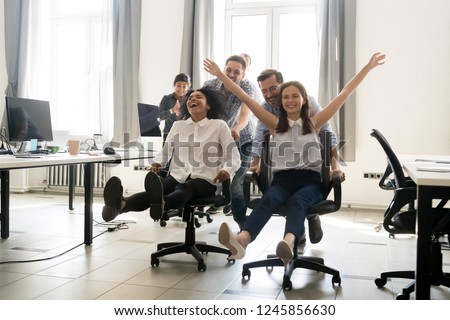 Happy multiracial colleagues group having fun together, riding on chairs in office, diverse excited office workers enjoying break, laughing, engaged funny activity, celebrating corporate success Royalty-Free Stock Photo #1245856630