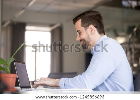 Smiling man using laptop, chatting in social network, typing on keyboard, looking at screen, businessman writing business email, economic report, browsing apps, doing online job, project, development