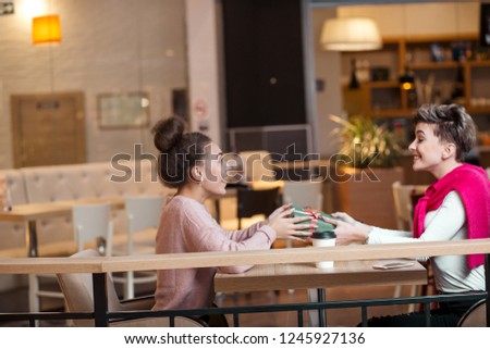 Happy caucasian woman congratulates her female friend with present box while sitting in mall cafe. Female friendship, girlfriends, holidays celebrating concept