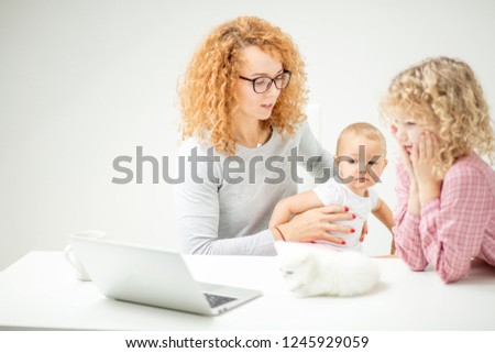angry mother is holding interfering little baby as she cannot do her work. woman is going to show a cartoon to her children . close up side view shot