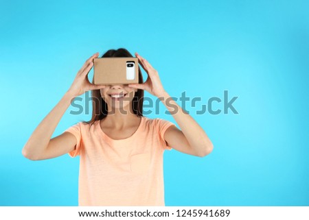 Young woman using cardboard virtual reality headset on color background. Space for text