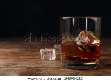 Golden whiskey in glass with ice cubes on table. Space for text