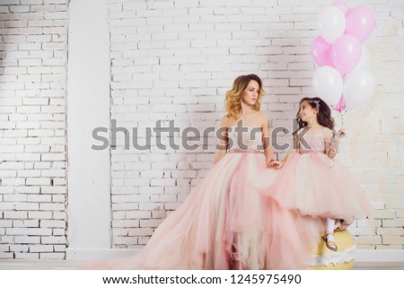 Mom and daughter in luxurious, pink, lush dresses. Family clothes, identical dresses. The background is beautiful, expensive, white, classic interior. Artistic, family photography.